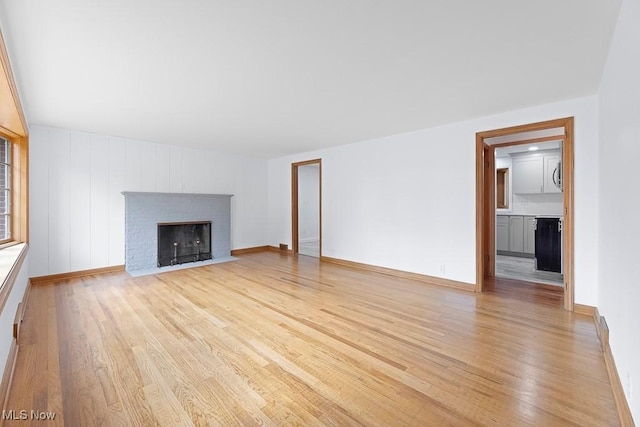 unfurnished living room featuring a brick fireplace, baseboards, and light wood finished floors