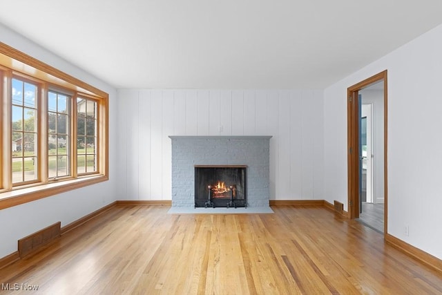 unfurnished living room with a brick fireplace, wood finished floors, visible vents, and baseboards