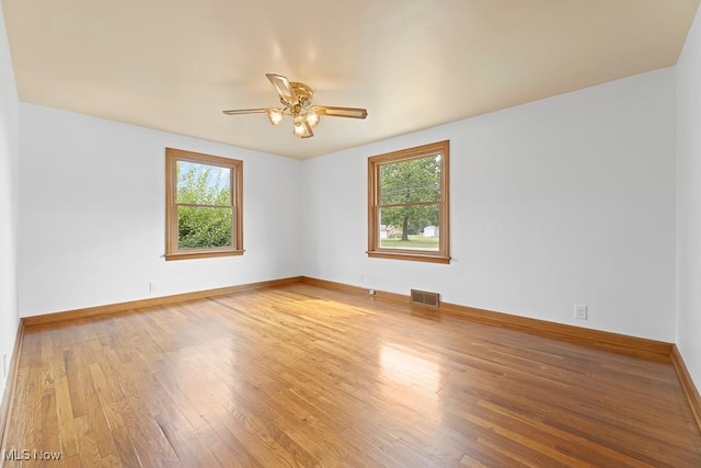 spare room featuring a ceiling fan, plenty of natural light, wood finished floors, and visible vents