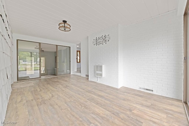 spare room with heating unit, visible vents, brick wall, and light wood-type flooring