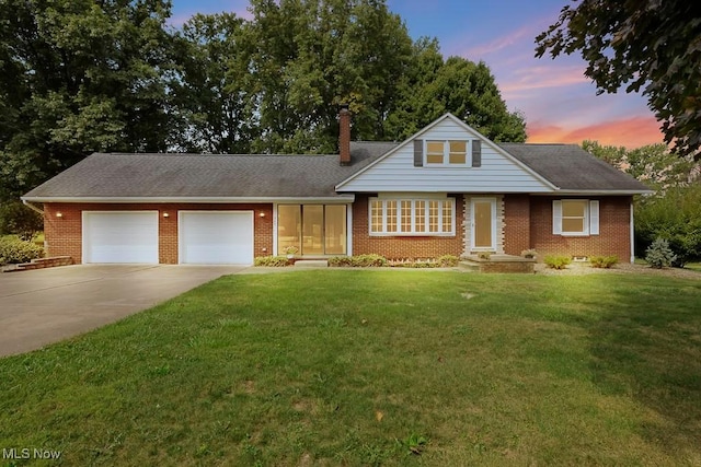 view of front of house with driveway, a yard, an attached garage, brick siding, and a chimney