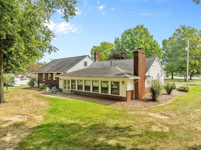 back of property with a yard, a shingled roof, a chimney, a patio area, and brick siding