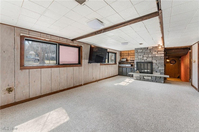 unfurnished living room featuring carpet, wooden walls, a fireplace, and baseboards