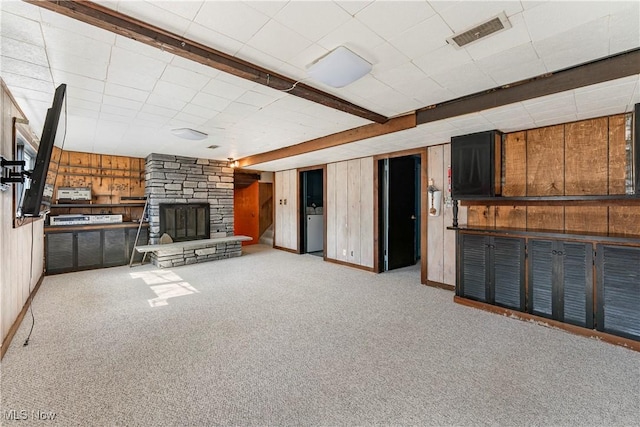 unfurnished living room with wooden walls, visible vents, washer / dryer, a stone fireplace, and carpet flooring