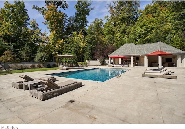 pool with a patio, fence, an exterior structure, a fire pit, and an outdoor structure