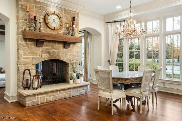 dining area featuring arched walkways, dark wood-style flooring, a stone fireplace, crown molding, and a notable chandelier