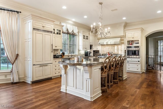 kitchen featuring a center island, oven, under cabinet range hood, a breakfast bar area, and arched walkways