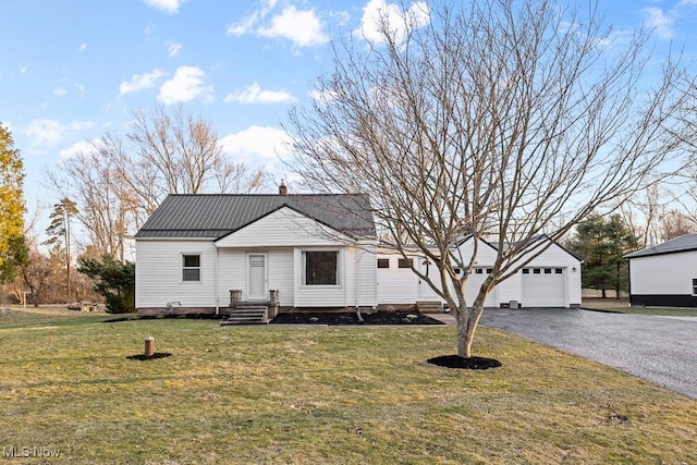 view of front of house featuring driveway, a front lawn, entry steps, a detached garage, and metal roof