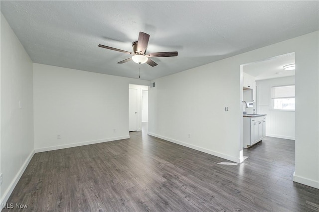 unfurnished room with dark wood-style floors, baseboards, a sink, ceiling fan, and a textured ceiling