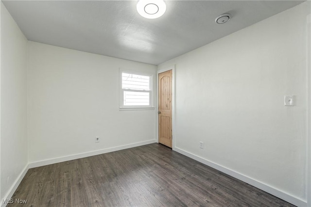 empty room with baseboards and dark wood-type flooring