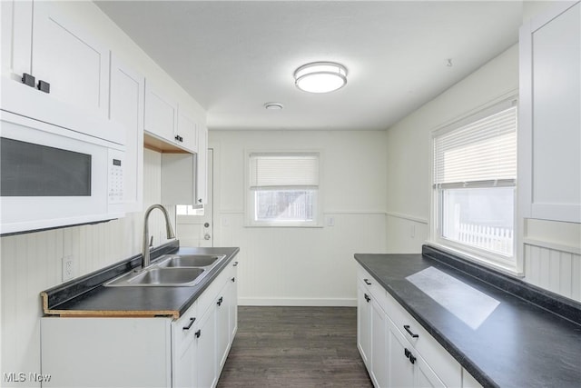 kitchen featuring dark wood-style floors, white microwave, a sink, white cabinets, and dark countertops