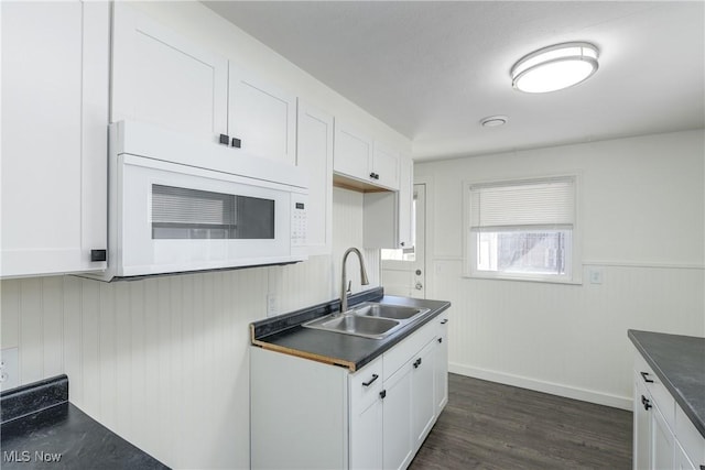 kitchen featuring white cabinetry, dark countertops, white microwave, and a sink