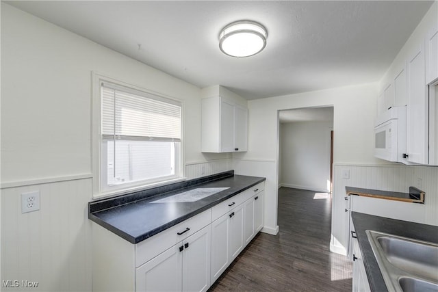 kitchen featuring white microwave, dark countertops, dark wood-type flooring, wainscoting, and white cabinetry