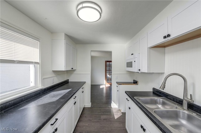 kitchen featuring dark countertops, white microwave, dark wood finished floors, white cabinets, and a sink