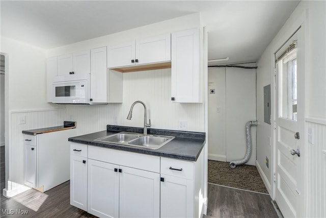 kitchen featuring a sink, white microwave, dark countertops, and dark wood-style floors