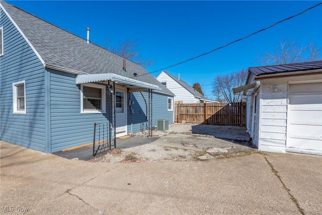 view of property exterior with central AC, fence, a garage, and roof with shingles