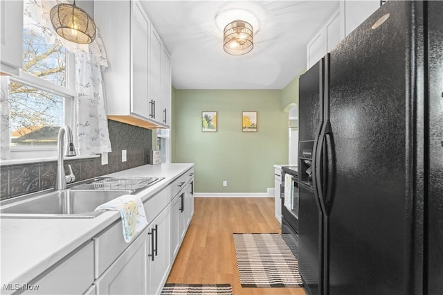 kitchen featuring a sink, decorative backsplash, light wood-style floors, white cabinetry, and black fridge