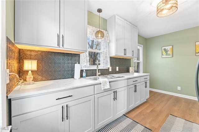 kitchen featuring a sink, light wood-style floors, light countertops, decorative backsplash, and baseboards