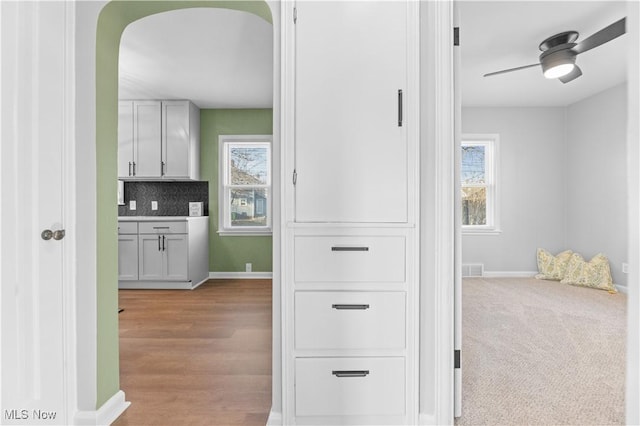 hall featuring visible vents, light carpet, arched walkways, light wood-style floors, and baseboards