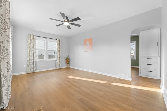 empty room with arched walkways, light wood-style flooring, a wealth of natural light, and a ceiling fan