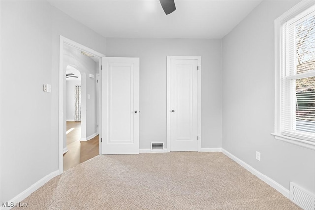 unfurnished bedroom featuring visible vents, baseboards, arched walkways, and carpet flooring