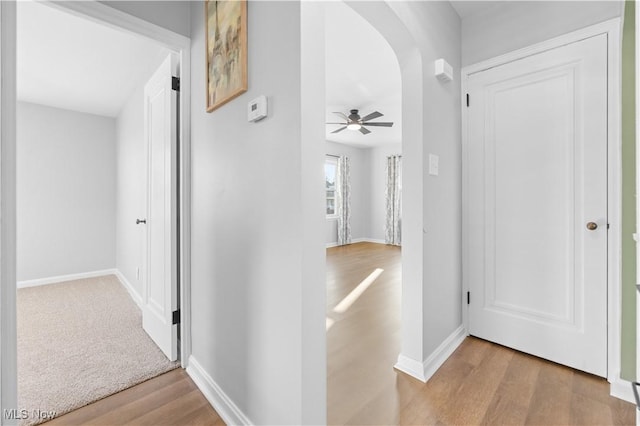 hall featuring baseboards, arched walkways, and wood finished floors