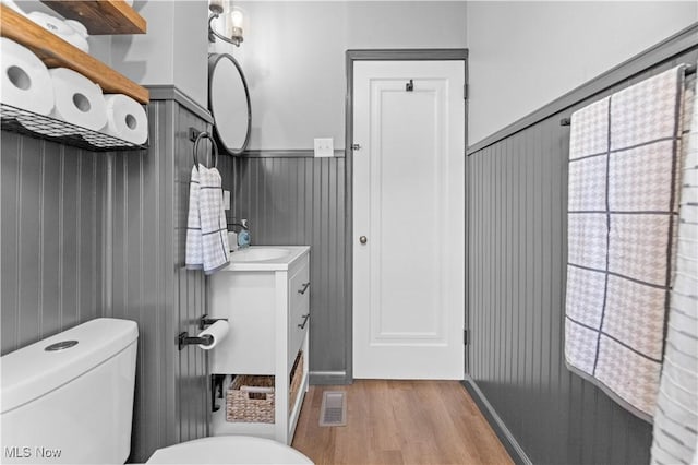 half bath with visible vents, a wainscoted wall, toilet, wood finished floors, and vanity