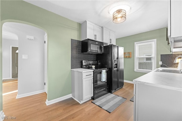 kitchen featuring a sink, arched walkways, black appliances, and light countertops