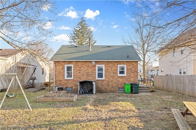 back of property with a lawn, fence, a vegetable garden, a shingled roof, and brick siding