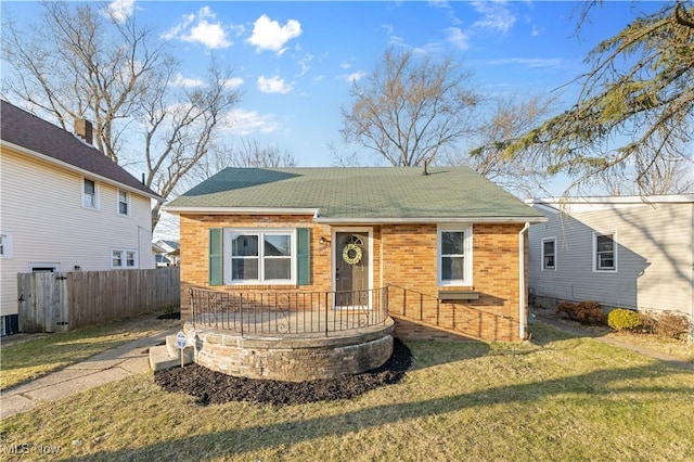 bungalow with brick siding, a shingled roof, a front lawn, and fence