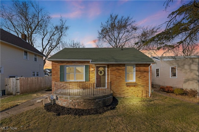 bungalow featuring a yard, fence, brick siding, and a shingled roof