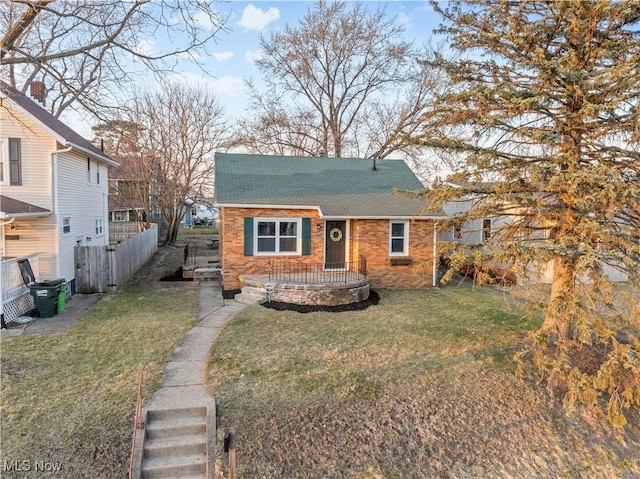 bungalow with a shingled roof, a front lawn, and fence