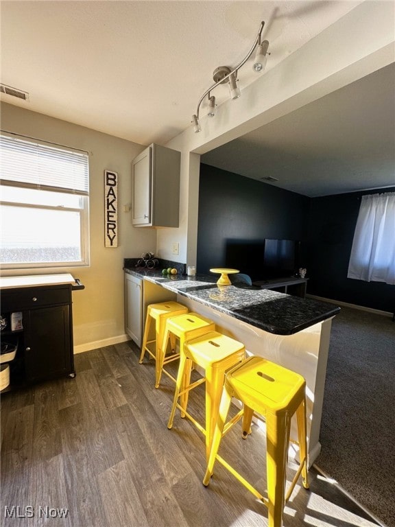 kitchen featuring visible vents, gray cabinets, dark countertops, baseboards, and dark wood-style flooring