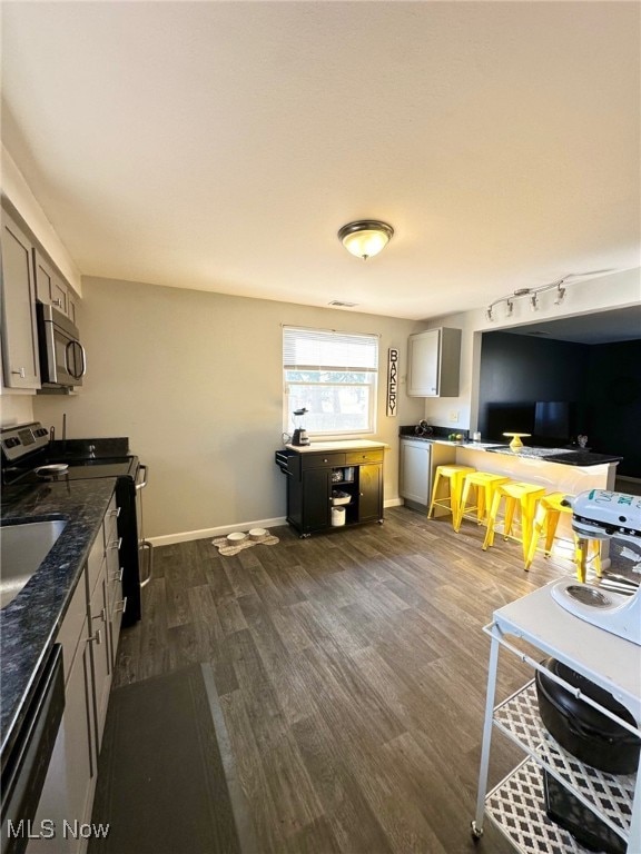 kitchen with dark wood-type flooring, a sink, dark stone counters, appliances with stainless steel finishes, and baseboards