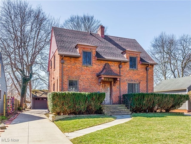 tudor home with an outbuilding, a front yard, a shingled roof, brick siding, and a chimney