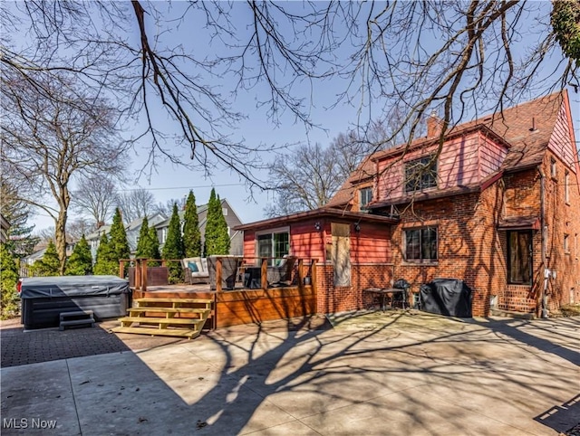 exterior space featuring a wooden deck, a patio, brick siding, and a hot tub