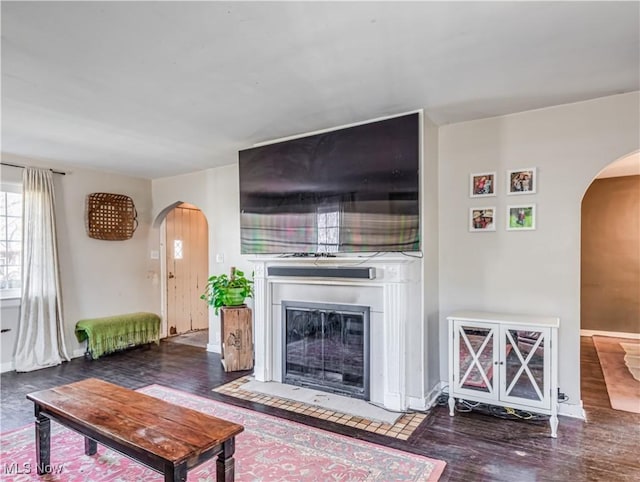 living room with a fireplace with flush hearth, wood finished floors, arched walkways, and baseboards