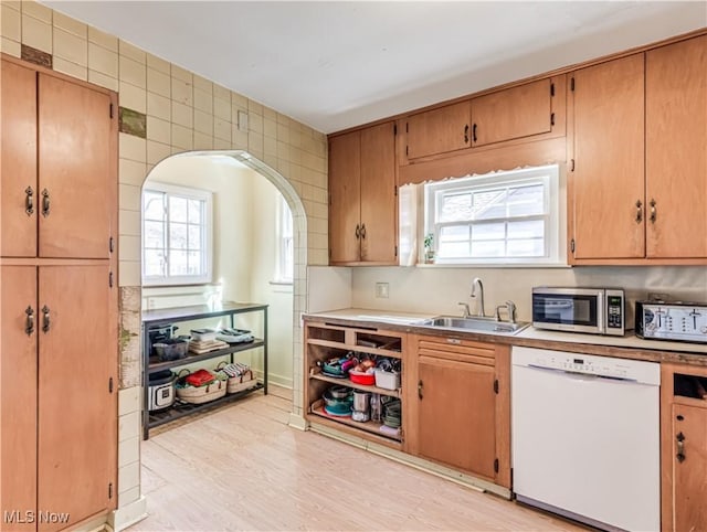 kitchen featuring light wood-style flooring, a sink, stainless steel microwave, arched walkways, and dishwasher