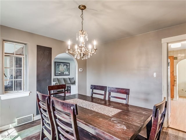 dining area featuring visible vents, wood finished floors, arched walkways, an inviting chandelier, and baseboards