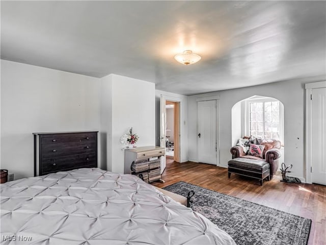 bedroom featuring wood finished floors and arched walkways