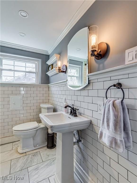 half bath with crown molding, toilet, a healthy amount of sunlight, and wainscoting