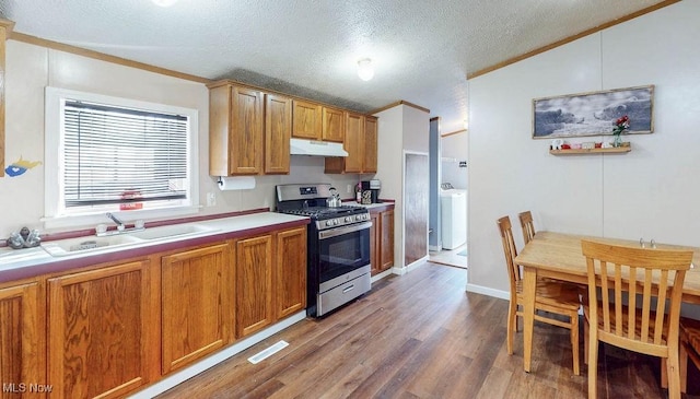 kitchen with a sink, under cabinet range hood, washer / clothes dryer, wood finished floors, and stainless steel range with gas stovetop