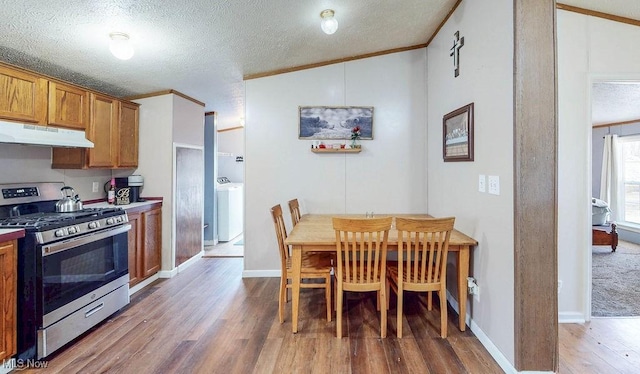 kitchen featuring brown cabinets, ornamental molding, under cabinet range hood, washer / dryer, and stainless steel range with gas stovetop