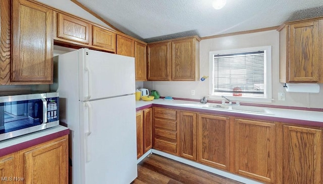 kitchen featuring lofted ceiling, freestanding refrigerator, a sink, stainless steel microwave, and brown cabinets