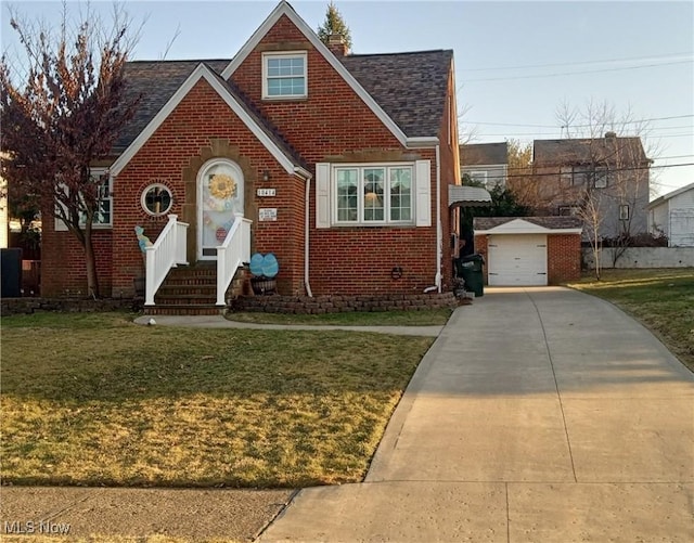 view of front of home with brick siding, a front lawn, concrete driveway, roof with shingles, and an outbuilding