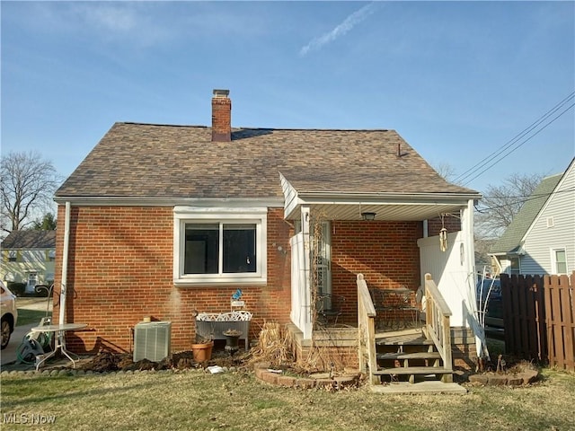 back of property with brick siding, a shingled roof, a chimney, and fence