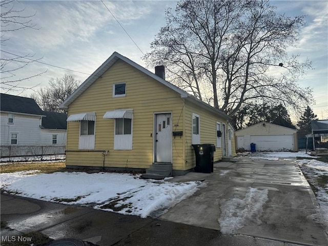 bungalow-style house with entry steps, an outdoor structure, a detached garage, and a chimney