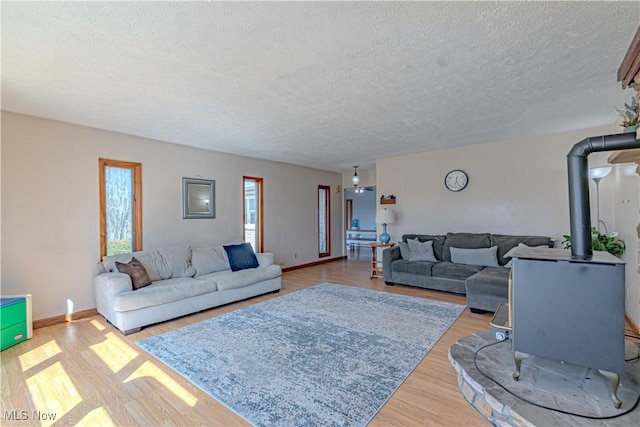 living room with a textured ceiling, a wood stove, baseboards, and wood finished floors