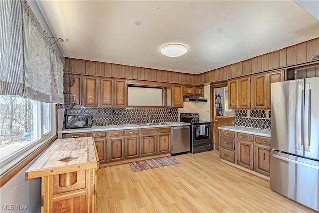 kitchen with brown cabinetry, light wood finished floors, a sink, under cabinet range hood, and appliances with stainless steel finishes