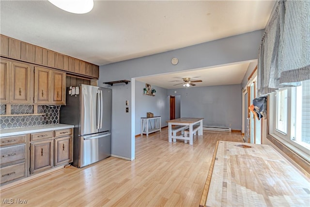 kitchen with light countertops, decorative backsplash, freestanding refrigerator, light wood-style floors, and brown cabinetry